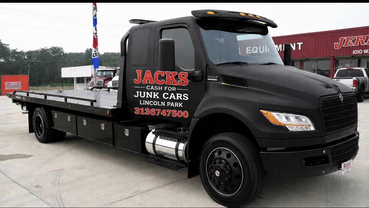 Matte black Jacks Cash for Junk Cars flatbed tow truck parked in a paved lot.